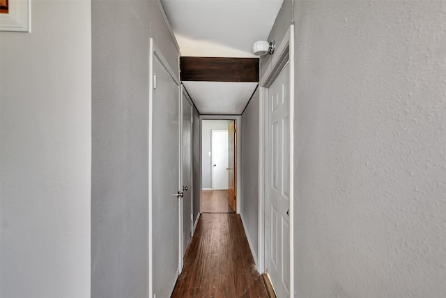 hallway featuring dark wood finished floors, baseboards, and a textured wall