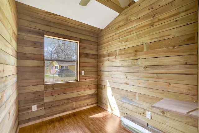 spare room with a ceiling fan, wood finished floors, wood walls, and vaulted ceiling