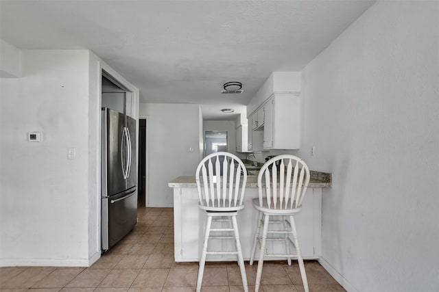 kitchen featuring light tile patterned floors, a peninsula, freestanding refrigerator, white cabinets, and a sink