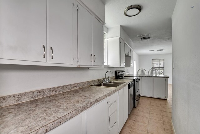 kitchen featuring visible vents, electric stove, a sink, light tile patterned flooring, and white cabinets