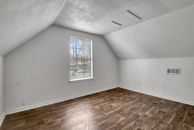 additional living space with dark wood-type flooring, baseboards, visible vents, and a textured ceiling