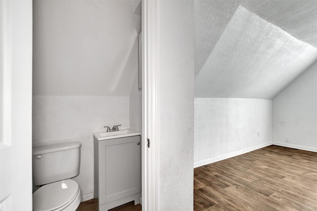 half bath featuring wood finished floors, baseboards, vaulted ceiling, a textured ceiling, and toilet