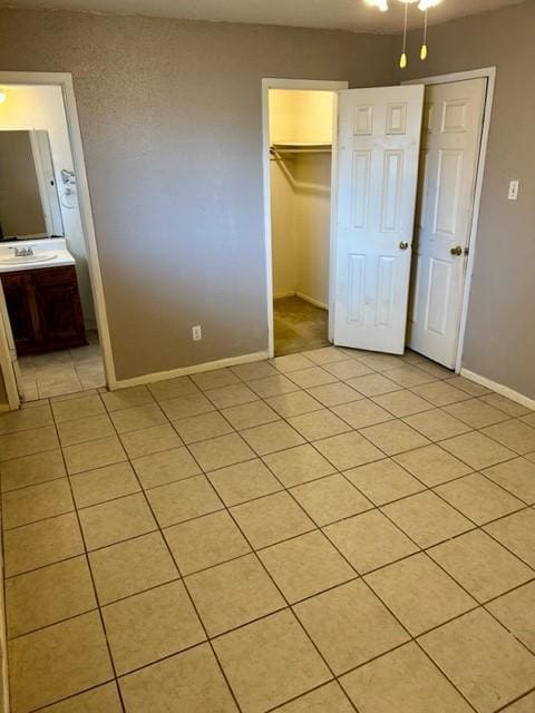 unfurnished bedroom with sink, light tile patterned floors, a walk in closet, and a closet