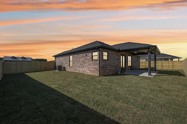 back house at dusk featuring a patio, central air condition unit, and a lawn