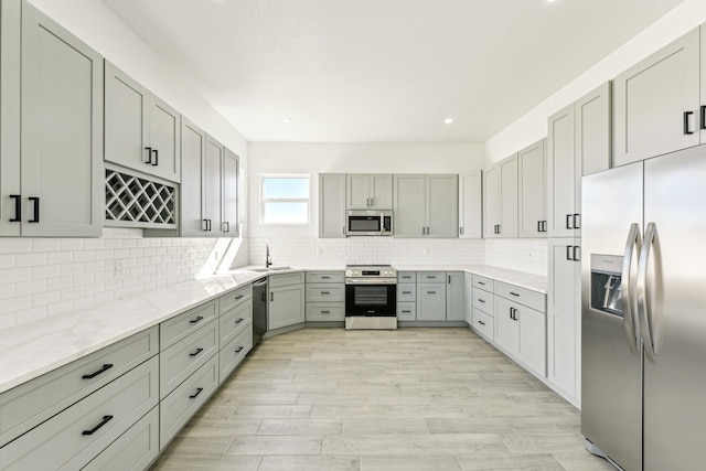 kitchen featuring decorative backsplash, light stone counters, stainless steel appliances, sink, and gray cabinets