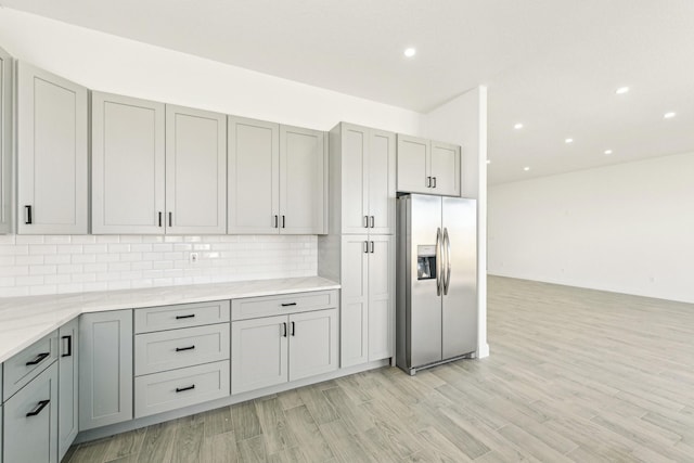 kitchen featuring light stone countertops, stainless steel fridge, backsplash, light hardwood / wood-style flooring, and gray cabinets