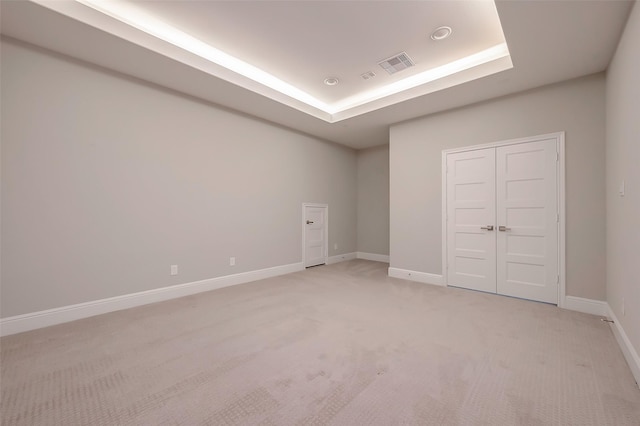 unfurnished bedroom with light colored carpet and a raised ceiling