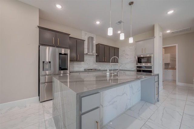 kitchen with pendant lighting, wall chimney exhaust hood, a large island, light stone counters, and stainless steel appliances