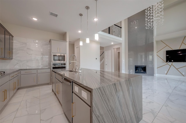 kitchen featuring appliances with stainless steel finishes, backsplash, a kitchen island with sink, sink, and hanging light fixtures