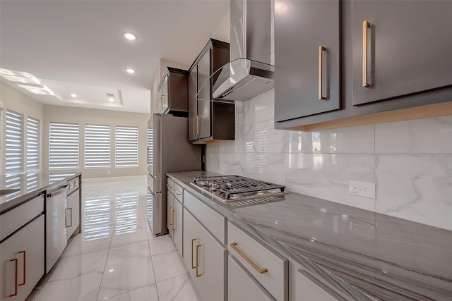 kitchen with wall chimney exhaust hood, light stone countertops, a tray ceiling, tasteful backsplash, and stainless steel appliances