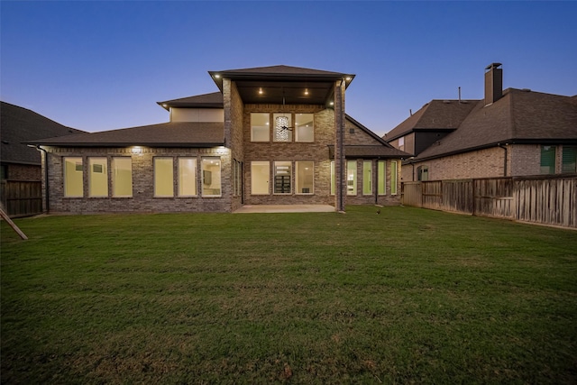 back house at dusk featuring a lawn