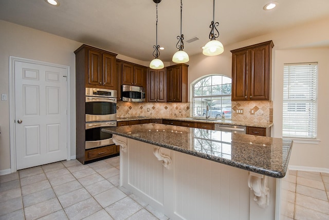 kitchen featuring decorative light fixtures, sink, dark stone counters, a center island, and stainless steel appliances