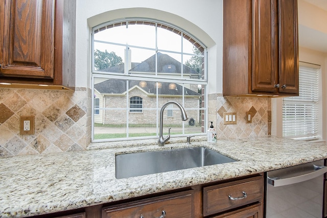 kitchen with sink, stainless steel dishwasher, a healthy amount of sunlight, light stone countertops, and decorative backsplash