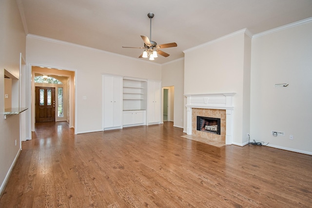 unfurnished living room featuring a tile fireplace, hardwood / wood-style floors, built in features, ceiling fan, and crown molding