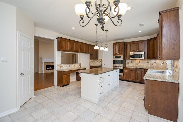 kitchen with a notable chandelier, a kitchen island, sink, appliances with stainless steel finishes, and light stone counters