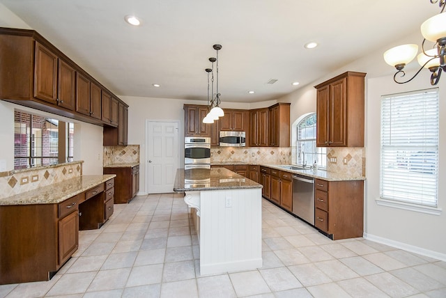 kitchen featuring appliances with stainless steel finishes, sink, hanging light fixtures, a center island, and light stone countertops