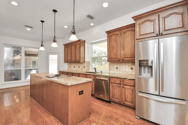 kitchen featuring a center island, stainless steel appliances, light stone counters, decorative light fixtures, and decorative backsplash