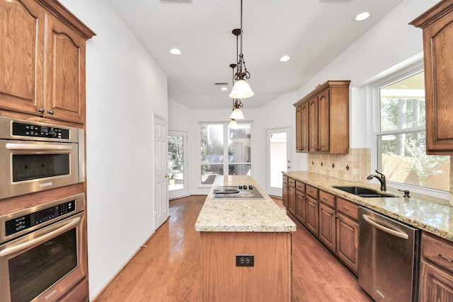 kitchen with light stone counters, stainless steel appliances, sink, pendant lighting, and a kitchen island