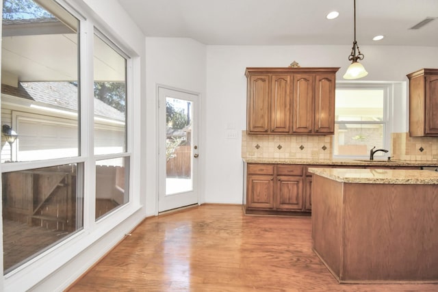 kitchen with backsplash, light stone countertops, hardwood / wood-style floors, and hanging light fixtures