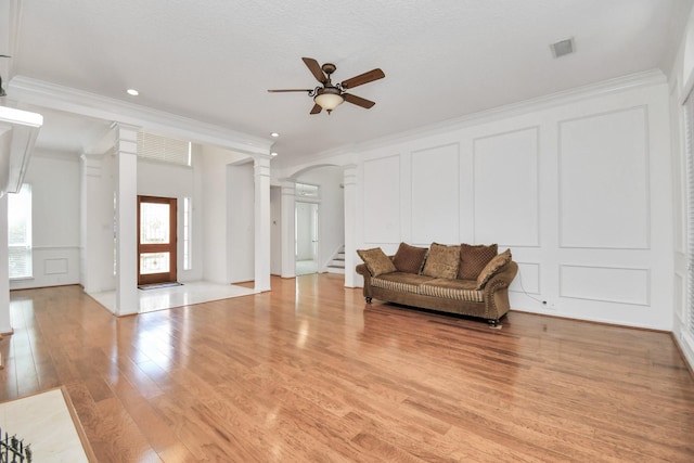 living room featuring ceiling fan, decorative columns, crown molding, light hardwood / wood-style floors, and a textured ceiling