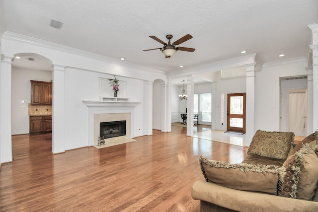 living room featuring ceiling fan with notable chandelier, crown molding, hardwood / wood-style flooring, a textured ceiling, and a tiled fireplace