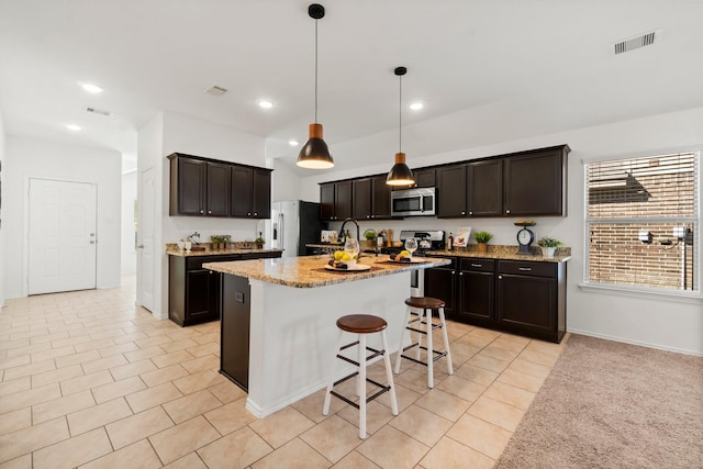 kitchen with a center island with sink, decorative light fixtures, light tile patterned flooring, light stone counters, and stainless steel appliances