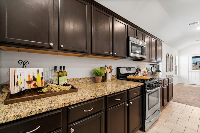 kitchen featuring light stone counters, vaulted ceiling, light carpet, dark brown cabinets, and appliances with stainless steel finishes