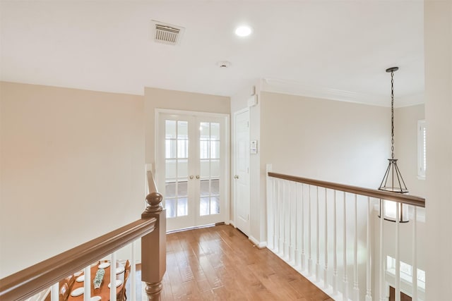 hall with light hardwood / wood-style floors, ornamental molding, and french doors