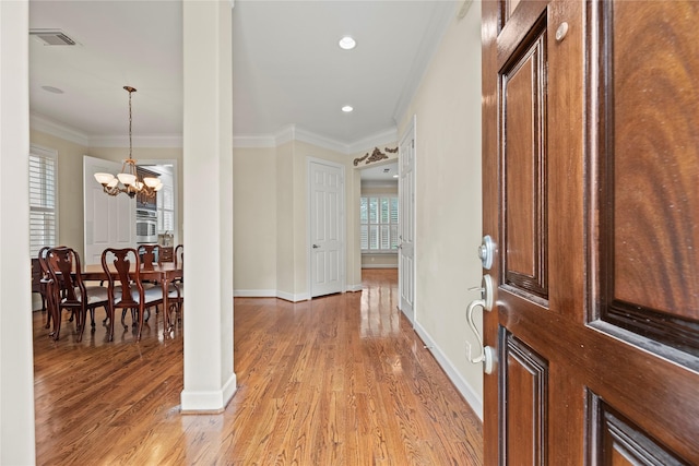 foyer featuring light wood-type flooring, crown molding, and a notable chandelier