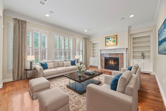 living room with built in shelves, ornamental molding, a fireplace, and light hardwood / wood-style flooring