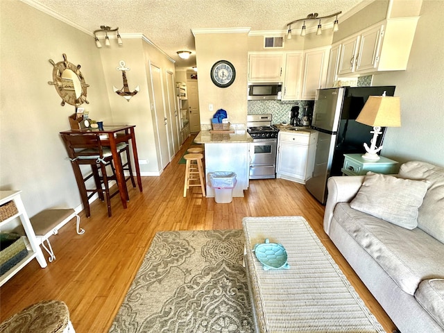 kitchen with a breakfast bar area, light wood-type flooring, white cabinets, stainless steel appliances, and backsplash