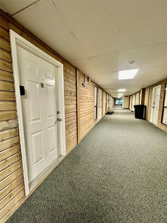 interior space featuring a paneled ceiling, carpet, and wood walls