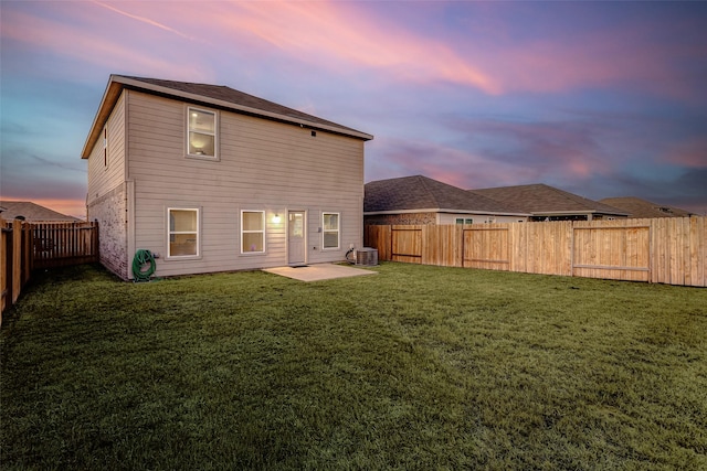 back house at dusk with central AC, a lawn, and a patio area