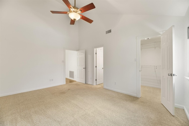 unfurnished bedroom with light carpet, ceiling fan, high vaulted ceiling, a spacious closet, and a closet