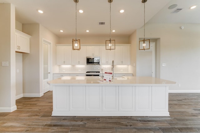 kitchen featuring white cabinets, decorative light fixtures, stainless steel appliances, and a kitchen island with sink