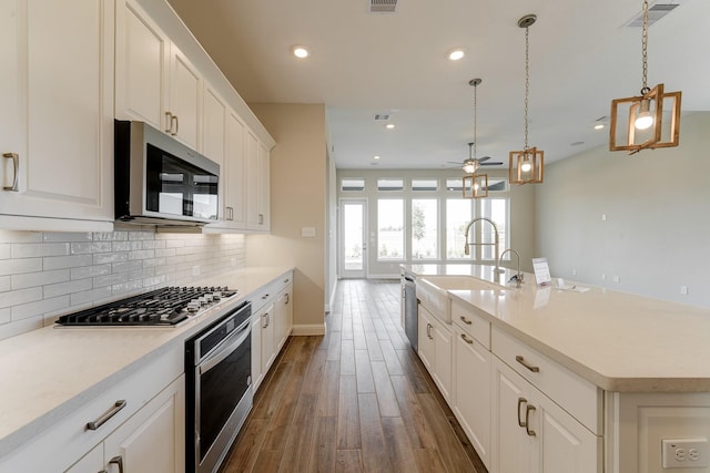 kitchen with dark wood-style flooring, stainless steel appliances, backsplash, white cabinets, and a sink