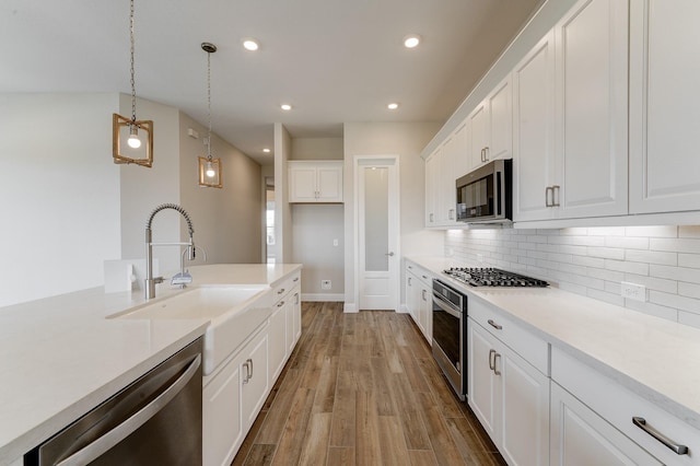 kitchen with light wood finished floors, decorative backsplash, appliances with stainless steel finishes, white cabinets, and a sink