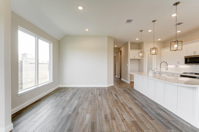 kitchen featuring visible vents, stainless steel microwave, light countertops, light wood-type flooring, and backsplash