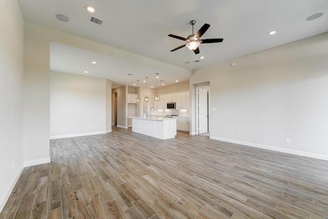 unfurnished living room with light wood-style floors, recessed lighting, visible vents, and a sink