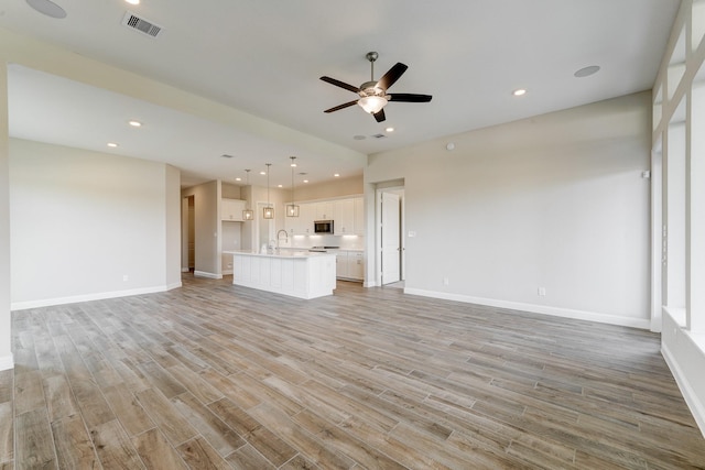 unfurnished living room with a ceiling fan, visible vents, a sink, and light wood-style flooring