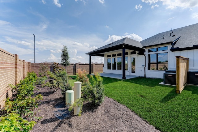 back of house featuring a shingled roof, a lawn, central AC unit, a patio area, and a fenced backyard