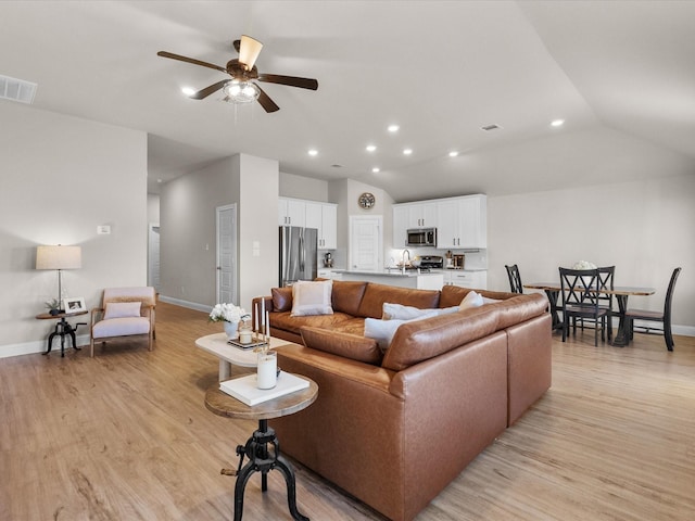 living room featuring ceiling fan, light hardwood / wood-style floors, and vaulted ceiling