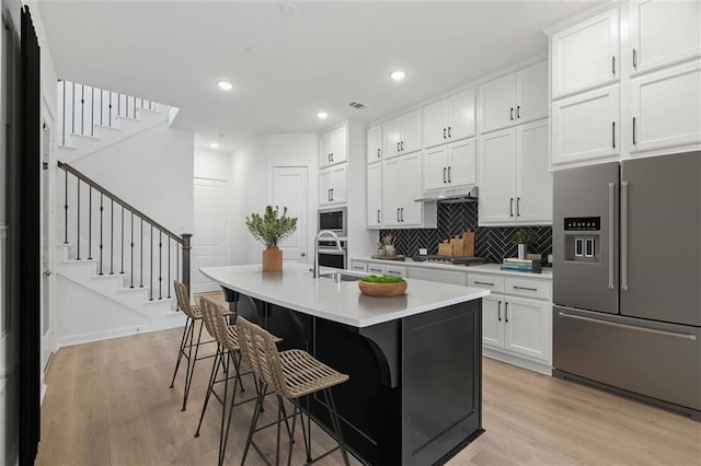 kitchen with a breakfast bar, a kitchen island with sink, white cabinets, light hardwood / wood-style flooring, and appliances with stainless steel finishes