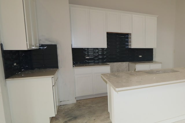 kitchen with decorative backsplash, concrete flooring, and white cabinetry