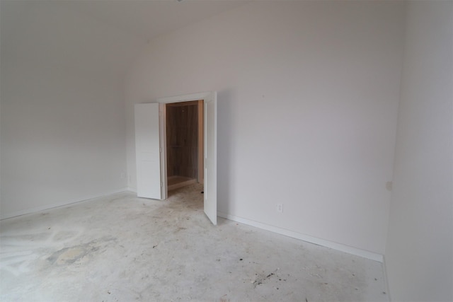 spare room featuring unfinished concrete floors, baseboards, and lofted ceiling