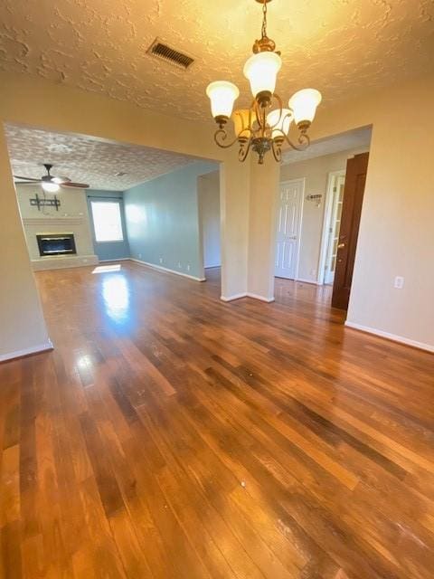 unfurnished living room featuring ceiling fan with notable chandelier, hardwood / wood-style floors, and a textured ceiling