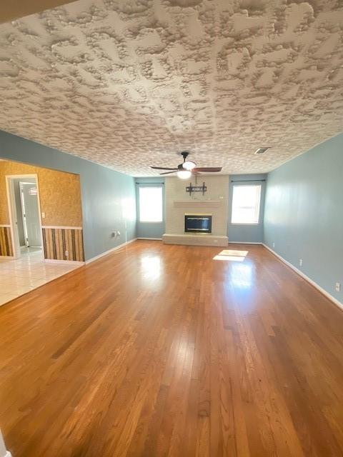 unfurnished living room with wood-type flooring, a wealth of natural light, and ceiling fan