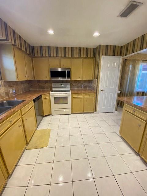 kitchen with sink, wood counters, backsplash, light tile patterned floors, and appliances with stainless steel finishes