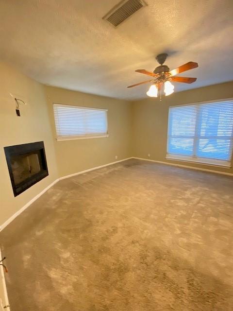 unfurnished living room with carpet flooring, a textured ceiling, and ceiling fan