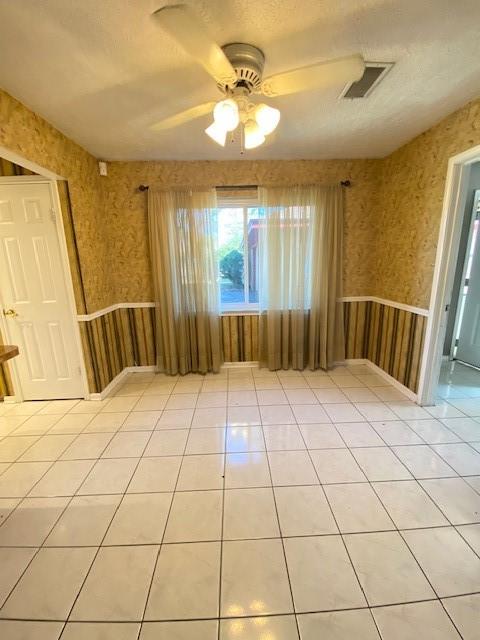 empty room featuring ceiling fan, light tile patterned floors, and a textured ceiling